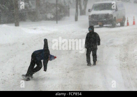 Staten Island, NY, USA. 23. Januar 2016. Menschen Sie Snowboard in der Mitte einer Straße Staten Island im Winter Sturm Jonas. Ein Reiseverbot hatte es seit Stunden, aber die Fähre noch betrieben. Schneefall Prognosen für Staten Island waren ca. 12-18 In mit Windgeschwindigkeiten in Böen bis zu 50 Meilen pro Stunde. Am späten Nachmittag Busse nicht mehr laufen und ein Reiseverbot wurde durch das NYPD durchgesetzt. Dieser Mangel an Verkehrsmitteln gestrandet viele Bewohner von Staten Island, die die Fähre nach Hause genommen hatte. Menschen waren gezwungen, zu versuchen, zu Fuß zu ihrem Bestimmungsort im Schneesturm. New Yorker Gouverneur Andrew Cuomo erklärte Stockfoto