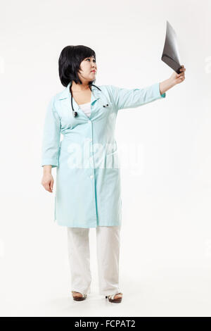 Kurvige Frau Doktor Stand hält die Ergebnisse der Radiologie, Röntgen Schädel Bild ausgestreckten Arm, in Türkis medizinische Kleid mit Stethoskop. Asiatischen aussehen, dunkle kurze Haare. Stockfoto