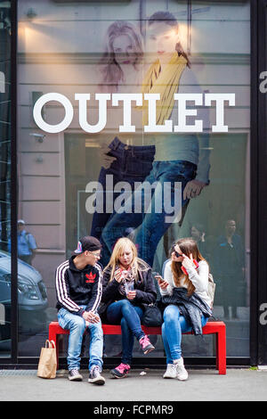 Outlet - drei junge Leute sitzen auf einer roten Bank außerhalb einer trendigen Berlin-Bekleidungsgeschäft Stockfoto