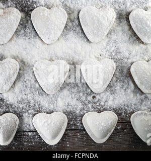 Ravioli kochen. Herzförmige Knödel, Mehl und Nudelholz auf hölzernen Hintergrund. Ansicht von oben. Stockfoto