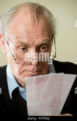 Ein älterer Mann blickt auf seine Brille verwirrt gewissermaßen auf Lottoscheine Stockfoto