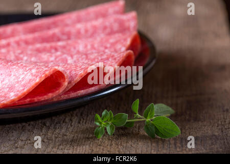 Salami-Scheiben auf schwarzen Druckplatte über hölzerne rustikalen Hintergrund Stockfoto