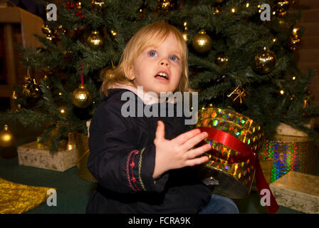 2 Jahre altes Mädchen sitzen um den Weihnachtsbaum mit Geschenken, Bordon, Hampshire, UK. Stockfoto