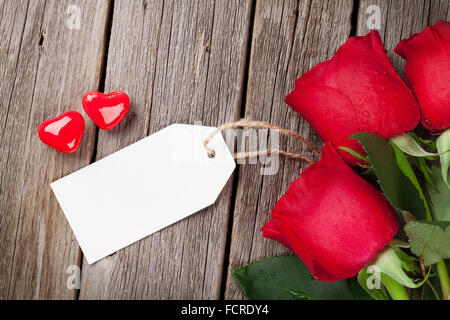 Rote Rosen mit Tag und Süßigkeiten Herzen über Holztisch. Valentinstag-Konzept Stockfoto
