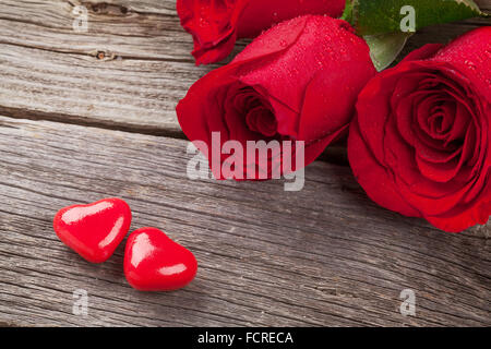 Rote Rosen und Zuckerherzen über Holztisch. Valentinstag-Konzept Stockfoto