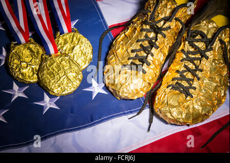 Goldene Schuhe sitzen neben einer passenden Sammlung von Goldmedaillen auf den roten, weißen und blauen Sternen und Streifen von einer amerikanischen Flagge Stockfoto