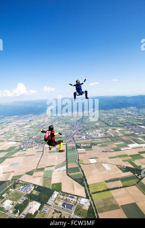 Zwei Freefly Fallschirmspringer bilden zusammen den Sit-Flug. Dabei fliegen sie mit über 120 km/h Geschwindigkeit in den blauen Himmel über Felder Stockfoto