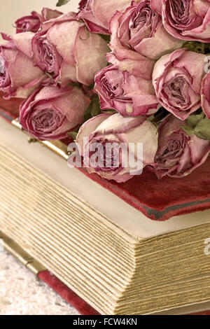 Bouquet von getrockneten Rosen auf dem alten Buch auf einem hölzernen Hintergrund Stockfoto