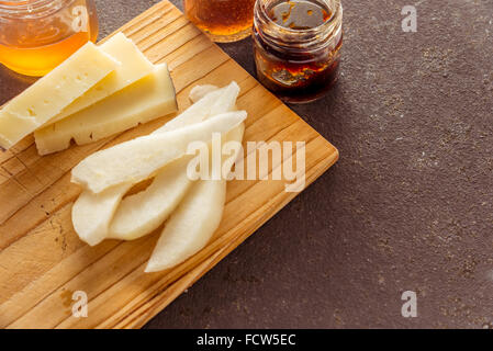 Eine Komposition aus italienischen Pecorino Käsescheiben mit Marmeladen und Birnen auf ein Schneidbrett aus Holz Stockfoto