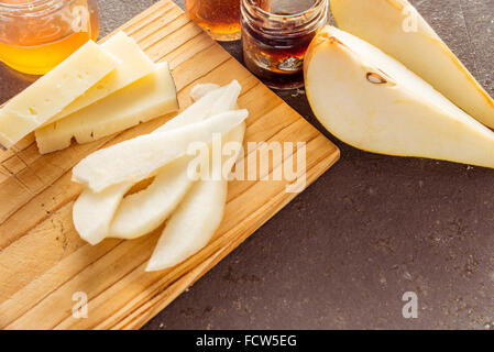 Eine Komposition aus italienischen Pecorino Käsescheiben mit Marmeladen und Birnen auf ein Schneidbrett aus Holz Stockfoto