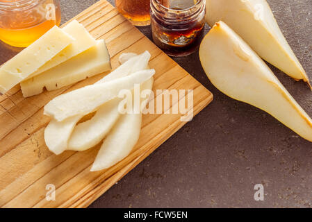 Eine Komposition aus italienischen Pecorino Käsescheiben mit Marmeladen und Birnen auf ein Schneidbrett aus Holz Stockfoto