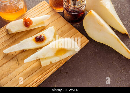 Eine Komposition aus italienischen Pecorino Käsescheiben mit Marmeladen und Birnen auf ein Schneidbrett aus Holz Stockfoto