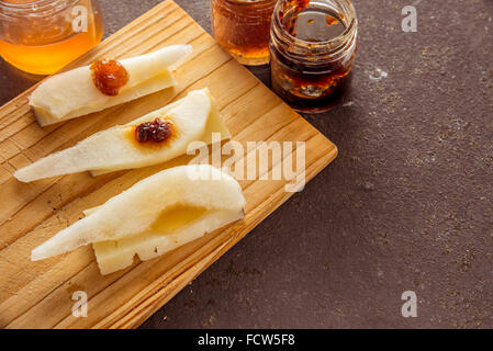 Eine Komposition aus italienischen Pecorino Käsescheiben mit Marmeladen und Birnen auf ein Schneidbrett aus Holz Stockfoto