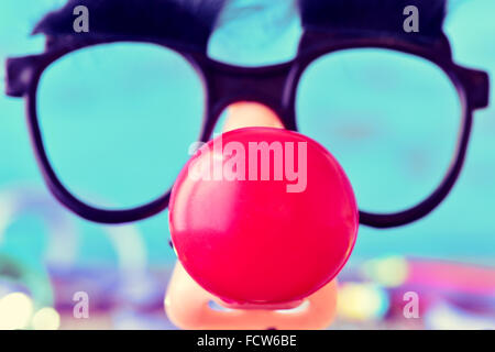Nahaufnahme von gefälschten schwarze Brille mit Augenbrauen und eine rote Clownsnase bilden das Gesicht eines Mannes, auf blauem Grund Stockfoto