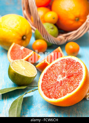 Scheiben von Grapefruit, verschiedene frische Zitrusfrüchte in einem Korb auf einem blauen Hintergrund aus Holz Stockfoto
