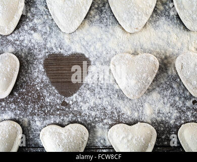 Herzförmige Ravioli mit Mehl, auf hölzernen Hintergrund bestreuen. Knödel kochen. Ansicht von oben. Ungekochten Ravioli Herzen Stockfoto