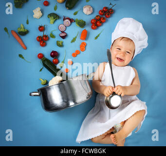 Baby Boy in Koch Hut mit Kochen Pfanne und Gemüse Stockfoto