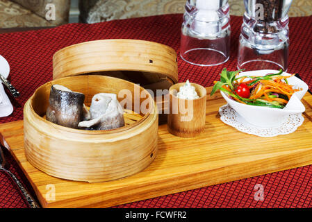 Geschirr, Holz Cup mit gedünstetem Fisch, Salat, Besteck. Kreative Küche. Stockfoto