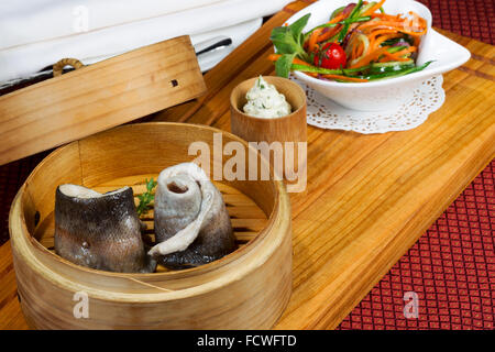 Geschirr, Holz Cup mit gedünstetem Fisch, Salat, Besteck. Kreative Küche. Stockfoto