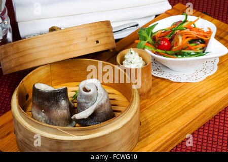 Geschirr, Holz Cup mit gedünstetem Fisch, Salat, Besteck. Kreative Küche. Stockfoto