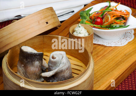 Geschirr, Holz Cup mit gedünstetem Fisch, Salat, Besteck Stockfoto