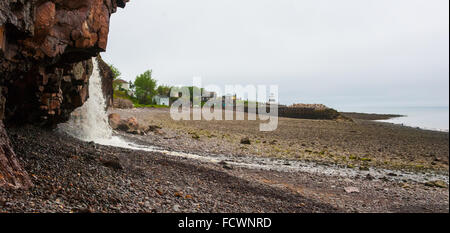 Frühling-Nova Scotia-Küste im Juni.   Wasserfälle von Klippe auf felsigen Kiesstrand. Stockfoto