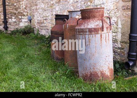 Nahaufnahme von drei rostigen alten Milchschürzen draußen auf dem Gras in England, Großbritannien Stockfoto