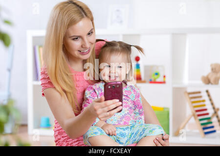 Mutter und ihr kleines Kind Mädchen nehmen Selfie auf einer Decke im Kinderzimmer Stockfoto