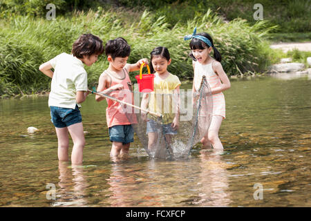 Vier Kinder, die Spaß für die Sommerferien in das Wasser des Baches halten ein Fischernetz und einen Eimer Stockfoto