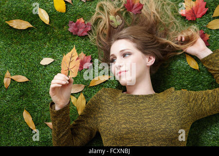 Porträt der jungen Frau mit langen Haaren auf dem Rasen mit Laub liegend Stockfoto