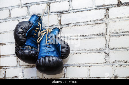 Ein paar der alten blauen und schwarzen Boxhandschuhen hängen weiße Ziegel Wand Hintergrund. Stockfoto