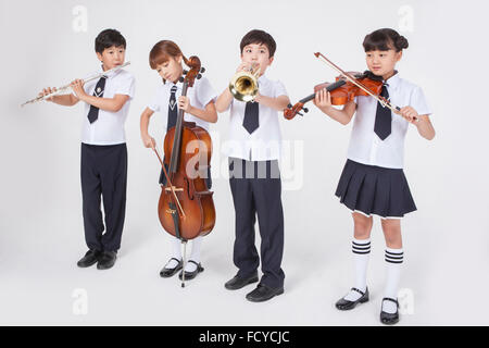 Vier Grundschüler in Schuluniformen stehen neben einander und spielen ein klassisches Musicals instrument Stockfoto