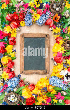 Ferien-Hintergrund mit Tafel. Frühling Blumen und Ostereier. Tulpen, Narzissen, Hyazinthen und Stiefmütterchen Blüten Stockfoto