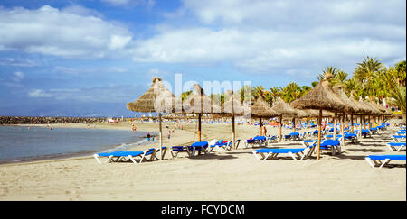 Teneriffa, Spanien - 18. Januar 2013: Stroh Sonnenschirme und Liegestühle am Playa de Las Americas, Teneriffa, Kanarische Inseln, Spanien Stockfoto