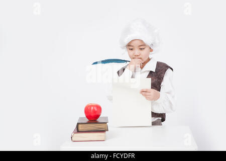 Junge im Stil klassischer Gelehrter mit einem Stück Papier und einen Stift Feder am Schreibtisch mit einem Apfel auf alte Bücher Stockfoto