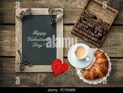 Kaffee mit Croissant, Blackboard und roten Herzen Dekoration. Romantischer Valentinstag Frühstück Stockfoto