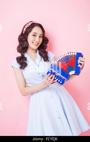Frau im Retro-Stil Mode hält ein Akkordeon mit einem Lächeln auf rosa Hintergrund Stockfoto