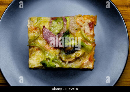 Stück Pizza mit Gemüse auf dem schwarzen Teller mit Messer und Gabel Stockfoto