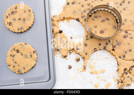 Chocolate Chip Cookies auf ein Backblech. Auf der Küchenarbeitsplatte ausgerollt mehr Kekse aus geschnitten Cookie-Teig. Stockfoto