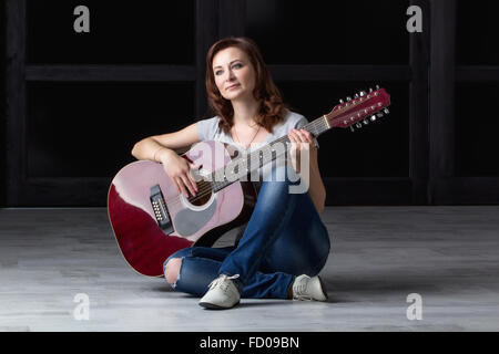 Mädchen mit Gitarre auf dem Boden sitzend Stockfoto