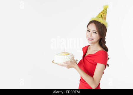 Frau im gelben Hut und roten Partykleid hält einen Kuchen und lächelnd nach vorne Stockfoto