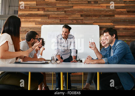 Gruppe der glückliche junge Menschen, die ein Business-Meeting. Kreative Leute sitzen am Tisch im Sitzungssaal mit Mann erklären busines Stockfoto
