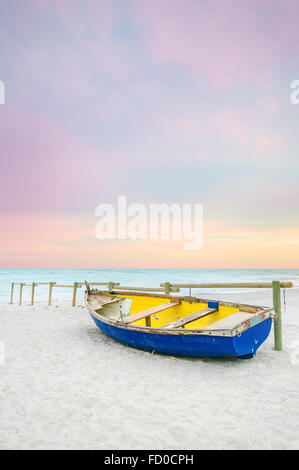 Tropische Seenlandschaft mit einem hölzernen, alt und kaputt gelb blau Boot auf weißen Strand im Sonnenuntergang. Stockfoto