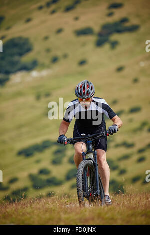 Radfahrer in voller Ausrüstung auf seinem Mountainbike bergauf gehen Stockfoto