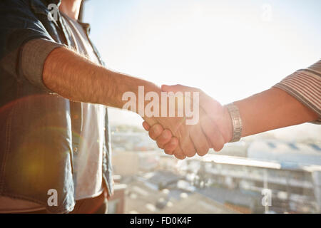 Nahaufnahme von zwei männlichen Händeschütteln mit Sonne Flare. Fokus auf Handschlag gegen Stadtbild. Stockfoto