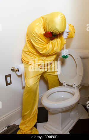 Frau, gekleidet in gelben Haz-Mat-Uniform und Ventilator Bad WC mit Bürste reinigen. Stockfoto