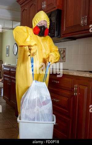 Frau in gelb Haz-Mat-Outfit gekleidet mit Ventilator herausnehmen den Müll in Küche. Stockfoto