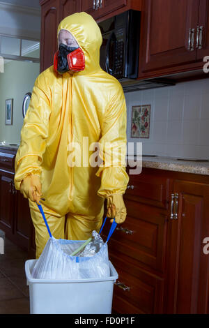 Frau in gelb Haz-Mat-Outfit gekleidet mit Ventilator herausnehmen den Müll in Küche. Stockfoto