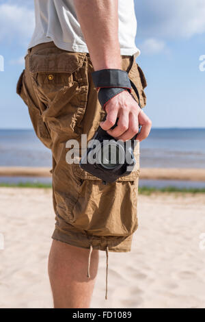 Mandressed in Hemd und Hosen, stehend auf dem sandigen Ufer des Meeres und Kamera halten. Stockfoto