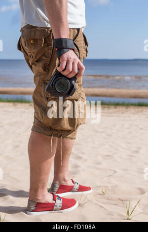 Mandressed in Hemd und Hosen, stehend auf dem sandigen Ufer des Meeres und Kamera halten. Stockfoto